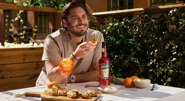 Man njuter av en solig stund med en läcker alkoholfri kaffedrink, tilltugg och en flaska Aperol.