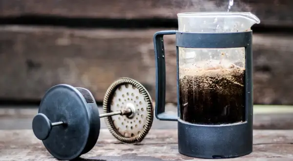 Varmt vatten hälls över kaffepulver i en presskaffe i kaffebryggare. Ånga stiger från den nybryggda drycken.