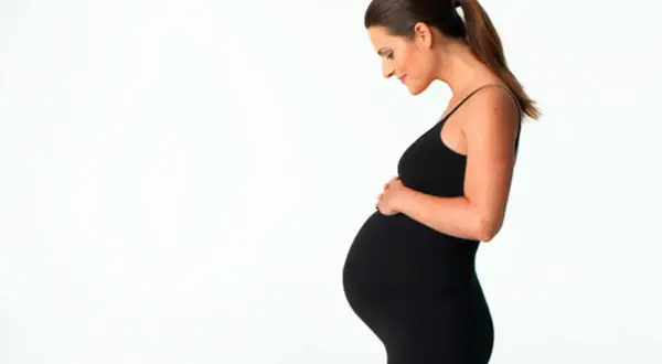 Gravid kvinna i svart klänning håller om sin mage. Hon ser lycklig ut, kanske hon funderar på att ta ginseng för energi.