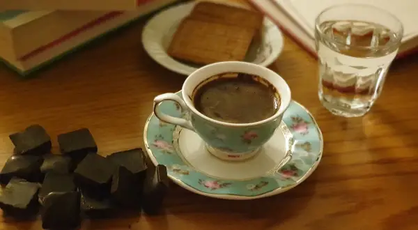 En kopp mörkt, aromatiskt kaffe med garvsyra, bredvid mörk choklad och en bok. En perfekt stund för avkoppling.