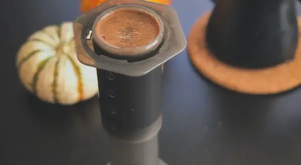 En kopp aeropress kaffe med en pumpa i bakgrunden.