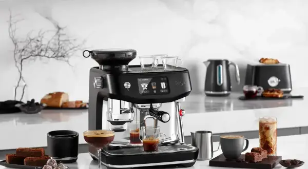 Snygg espressomaskin med inbyggd kvarn, som förbereder vanligt kaffe. Bredvid står godsaker och en kaffekopp.