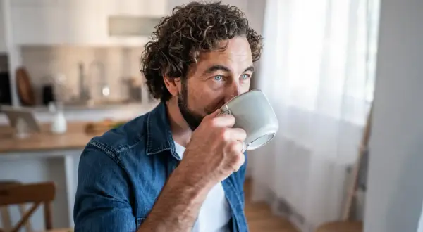 Man med lockigt hår dricker kaffe, blicken fundersam. Kanske en stund av kaffe ångest innan dagen börjar.