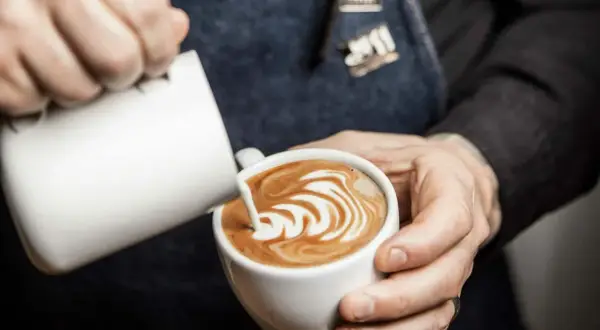 Barista skapar vacker latte art genom att hälla mjölk i en kaffekopp.