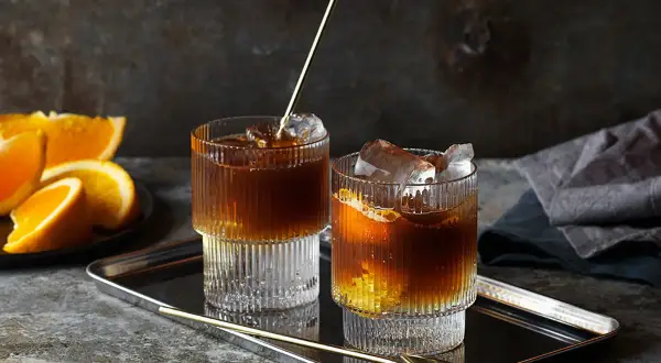 Två glas med kaffe tonic, is och apelsinskivor på ett fat.