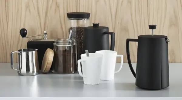 Kaffebönor och malet kaffe i glasburkar, en kaffekvarn, två vita muggar och två svarta presskannor. Perfekt för att utforska olika presskaffe sorter.