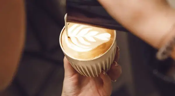 En barista skapar vackert latte art i en kopp kaffe latte.