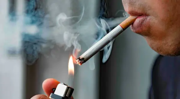 En person tänder en cigarett med en tändare. Röken virvlar. Hur många gram tobak i en cigarett är en fråga som många undrar över.