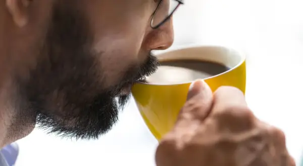 Man med glasögon dricker kaffe ur en gul mugg, känner koffein effekten.
