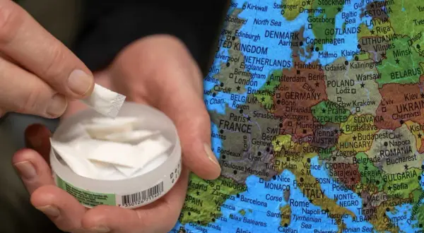 En hand håller en prilla snus framför en karta över Europa, med fokus på Danmark och Sverige. Copenhagen snus Sverige.