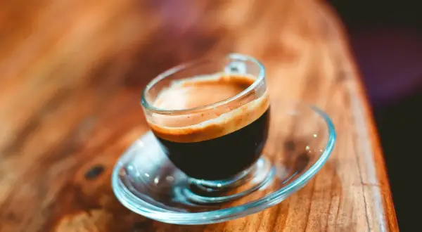 En kopp med en gyllene crema, en perfekt lungo kaffe, står på ett träbord.