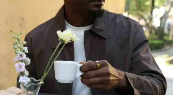 Man med guldig ring håller en vit kopp med te. Koffein ger energi för dagen.