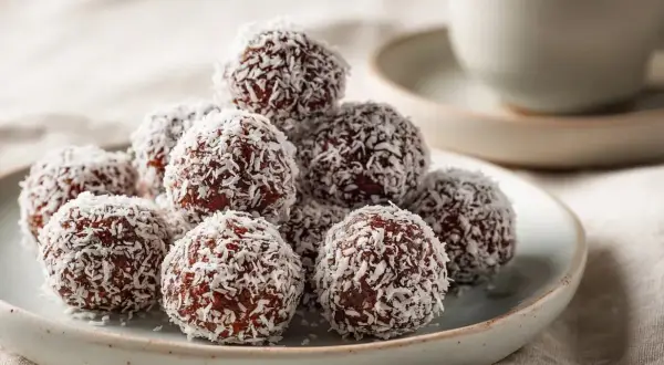 En hög med chokladbollar täckta av kokosflingor, redo att avnjutas med en kopp kaffe.