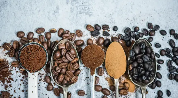 Fem skedar visar olika stadier av kaffe produktion: från hela bönor till fint malet pulver.
