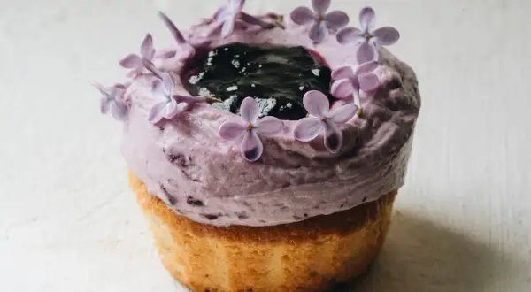 En lila cupcake med blåbärsfrosting, mörka bär och syrenblommor. Ett recept inspirerat av Starbucks.