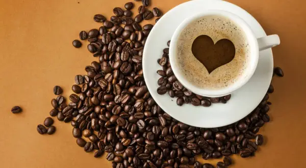 En kopp kaffe med ett hjärta i skummet, omgiven av kaffebönor. En visuell förklaring till hur fungerar koffein.