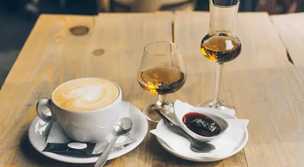 En kopp kaffe med vitt hjärta på skummet, bredvid två glas med bärnstensfärgad dryck och en skål med sylt. En perfekt kombination för en stunds njutning.