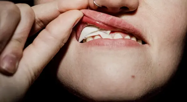 En person tar bort en snusprilla från munnen. Kanske är personen allergisk mot snus och upplever irritation.