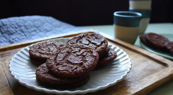 Chokladkakor på en vit tallrik, redo som en snabb kaka till kaffet. Bredvid står staplade muggar.
