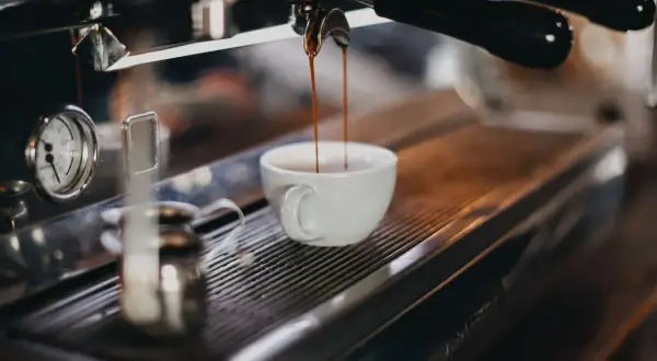 Espresso rinner ner i en vit kopp. En liten mjölkkanna står bredvid, redo för att skapa perfekt kaffeskum.