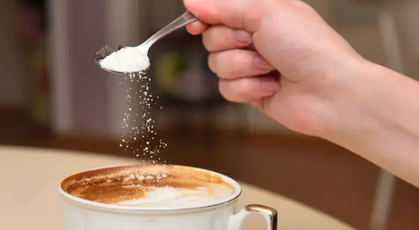 En hand häller socker från en sked ner i en kopp kaffe. Kanske är det salt i kaffet istället för socker?