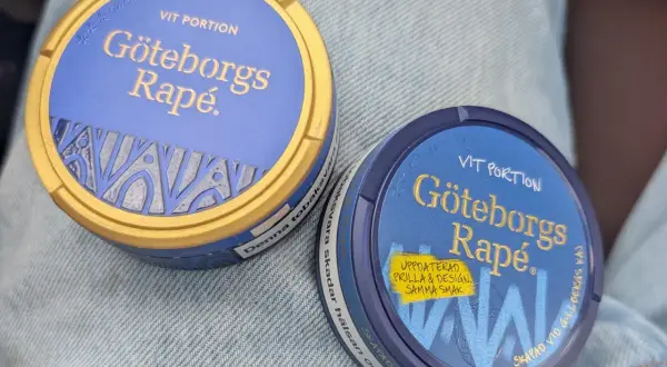 Två dosor Göteborgs Rapé, en med guldig kant, ligger på jeans. Perfekt för dig som vill ha snus som inte rinner.