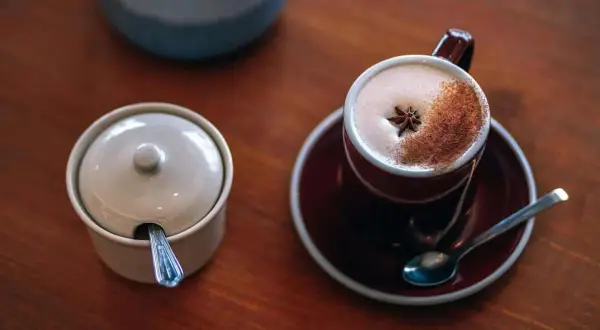 En kopp värmande chai latte med stjärnanis och kanel, bredvid en sockerskål med sked.