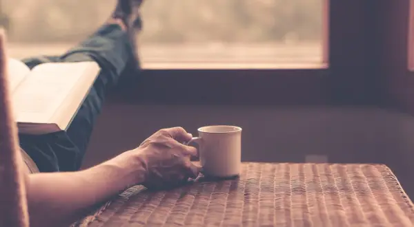 En person läser en bok med en kopp kaffe, njuter av stunden och funderar över kaffe ursprung.