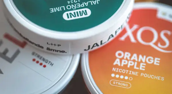 Tre dosor nikotinpåsar: en grön med jalapeño lime, en vit med texten "strength" och en orange med smak av apelsin och äpple. Frågan "hur många prillor i en dosa" kan besvaras genom att titta på dessa.