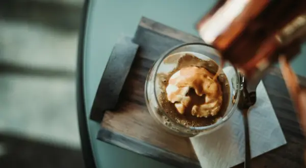 Varm espresso hälls över vaniljglass i en klassisk cafe affogato. En sked ligger bredvid.