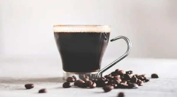 En kopp mörkt kaffe med skum och kaffebönor. Vitt te nyttigt, men en kopp kaffe ger också energi.