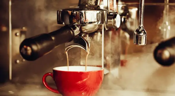En röd kopp fylls med rykande espresso från en maskin. En klassisk italiensk kaffeupplevelse.