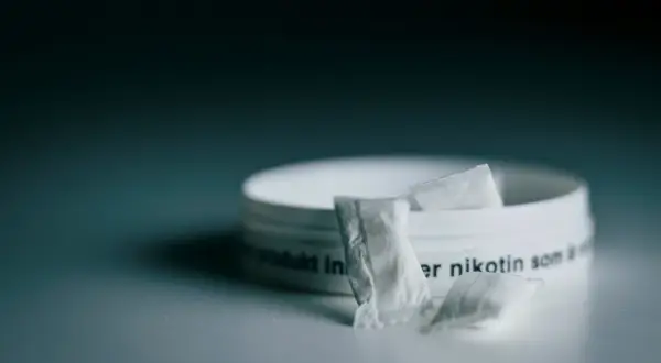 En dosa snus, ett populärt naswar i Sverige, med några påsar framför.