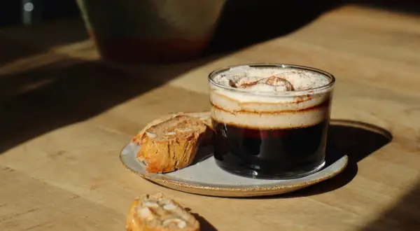 En lyxig kaffe creme med vispad grädde och kanel, serverad med mandelkakor på en träyta.
