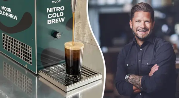 En leende man med tatueringar på armen bredvid en maskin som gör nitro cold brew.