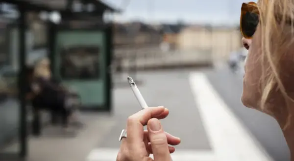En kvinna röker en cigarett vid en busshållplats. Bilden kan illustrera prisutveckling cigaretter.