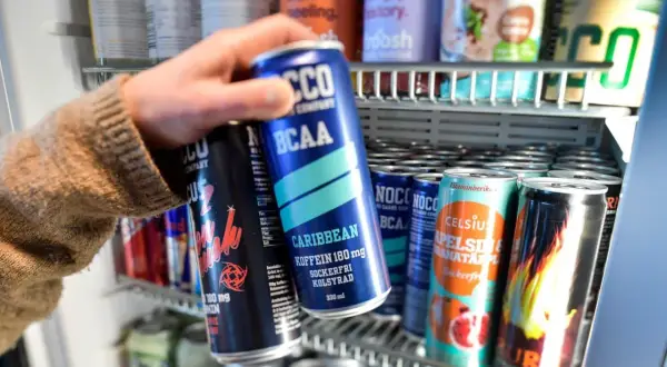Hand tar en energidryck ur ett kylskåp. Frågan om att dricka energidryck gravid är relevant.