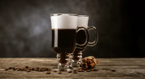 Två glas med krämig cappuccino, kaffebönor och kanelstänger. Perfekt för ett mysigt cappuccino recept.