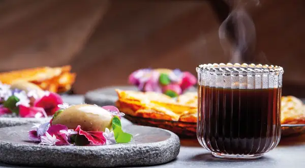 En ångande kopp kaffe glass serveras med en elegant dessert.