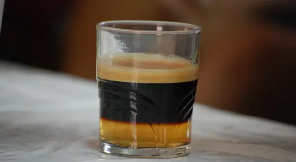 En spansk kaffedrink med lager av kaffe och skum i ett glas.