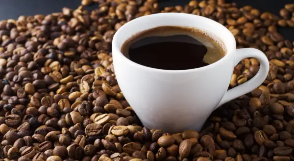 En vit kopp med mörkt, ångande kaffe omgiven av grovmalet kaffe. En perfekt start på dagen.