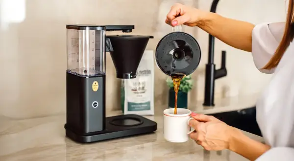 En kaffebryggare som visar hur fungerar en kaffebryggare, med nybryggt kaffe som hälls upp i en mugg.