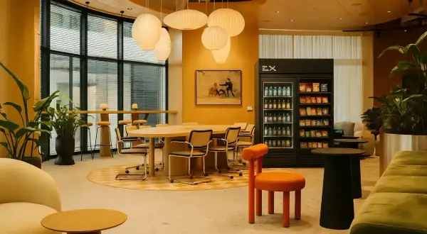 En modern arbetsplats med bekväma sittplatser, ett stort bord och en kyl med snacks, perfekt för en fika på jobbet.