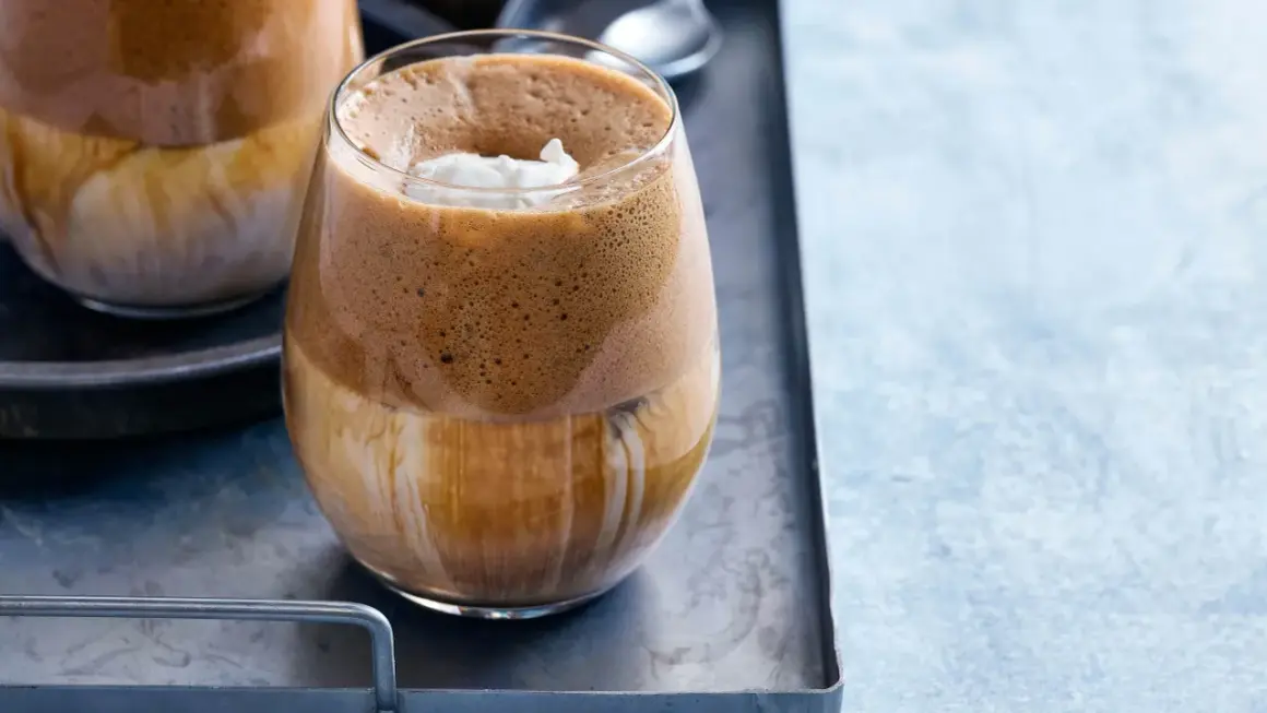 En glas med grekisk frappe, fylld med is och toppad med grädde.