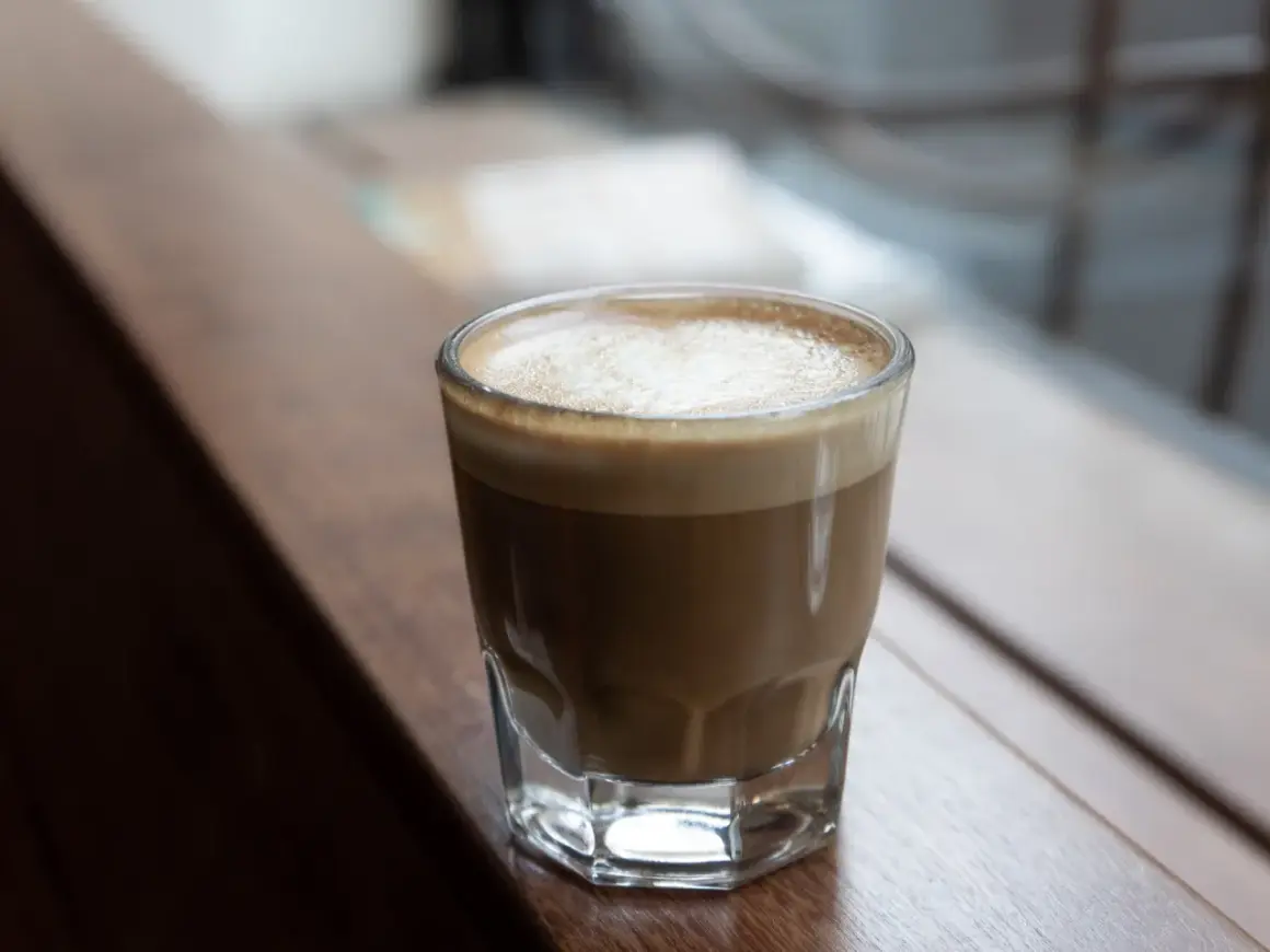 En perfekt cortado macchiato med krämigt skum, serverad i ett glas på en träyta.
