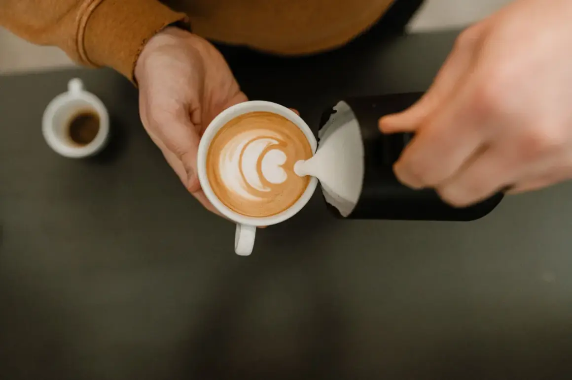 Barista häller mjölkskum i en kopp kaffe för att skapa lattekonst. Vad betyder latte? En kaffedryck med espresso och ångad mjölk.