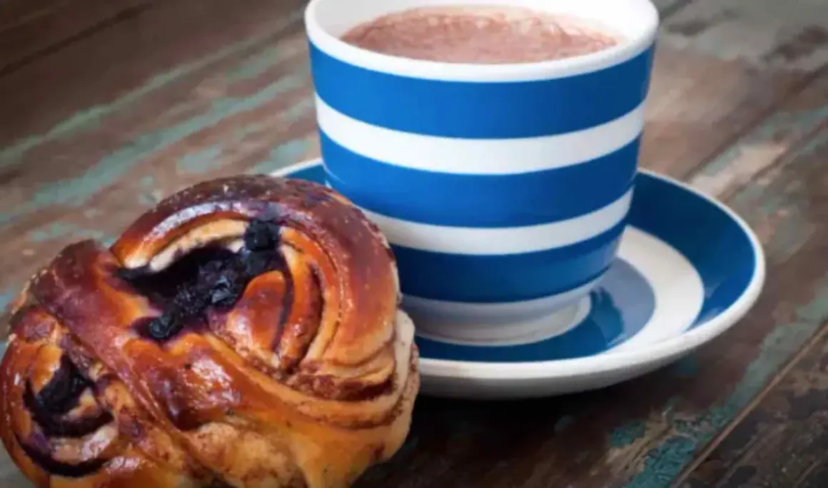 En blårandig kopp med kaffe och en kanelbulle med blåbär. Perfekt för en fika till jobbet.