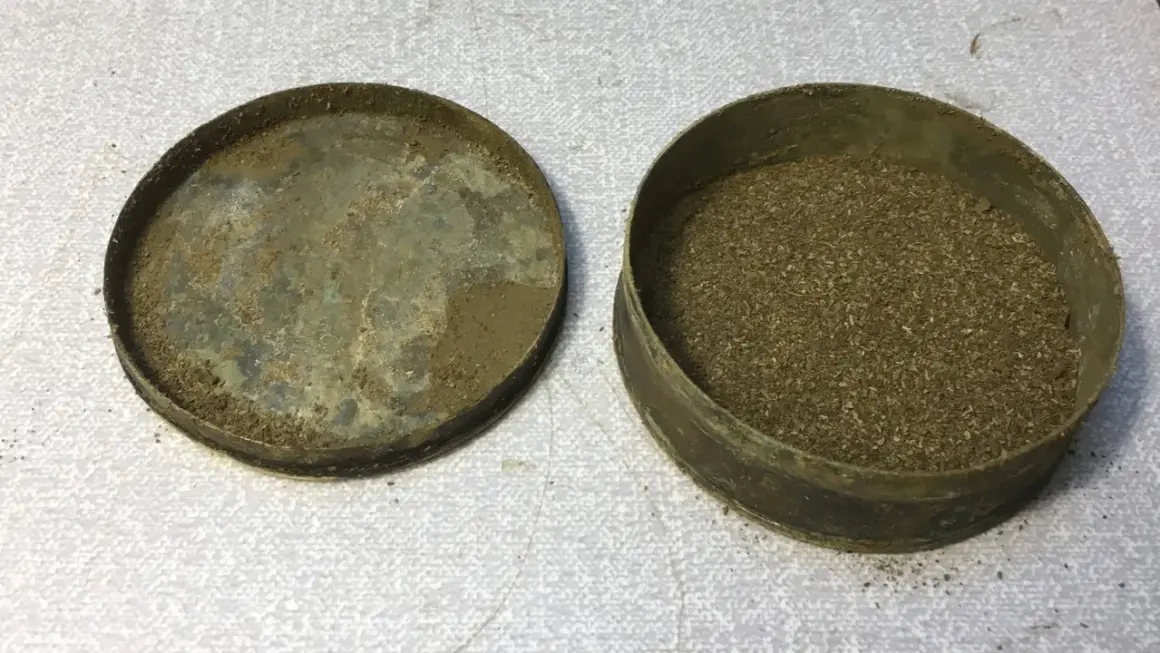 En gammal snusdosa med lock bredvid, fylld med utgånget snus.