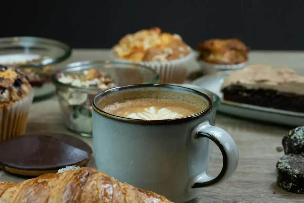 En kopp kaffe med lattekonst, en croissant och olika bakverk. En påminnelse om vart kommer kaffe ifrån och njutningen det ger.