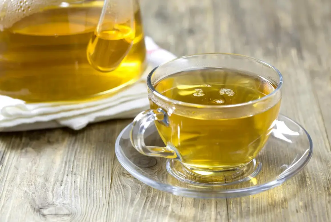 En kopp gyllene kamomillte, utan koffein, står på ett fat bredvid en tekanna.